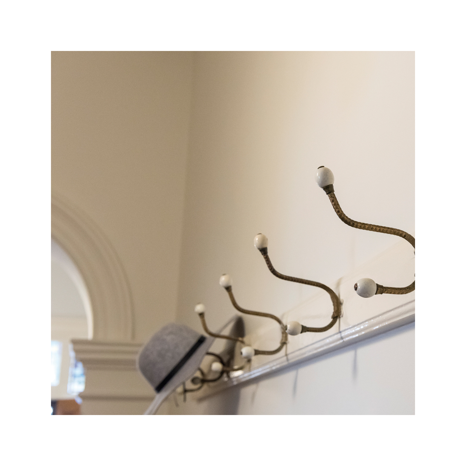 Vintage-style brass coat hooks with white ceramic tips mounted along a painted timber rail in a classic hallway.