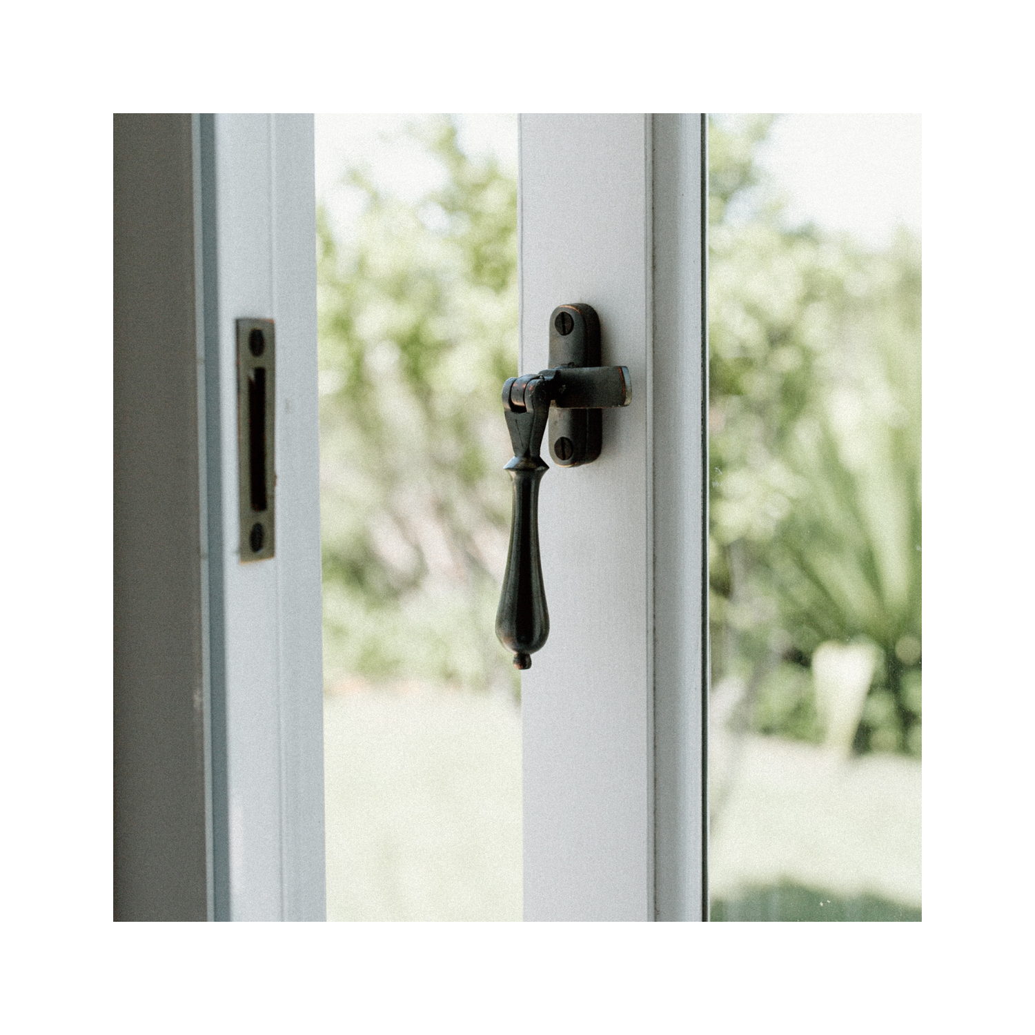 Classic casement window with painted timber frames and traditional aged brass window fastener, looking out to a garden beyond.