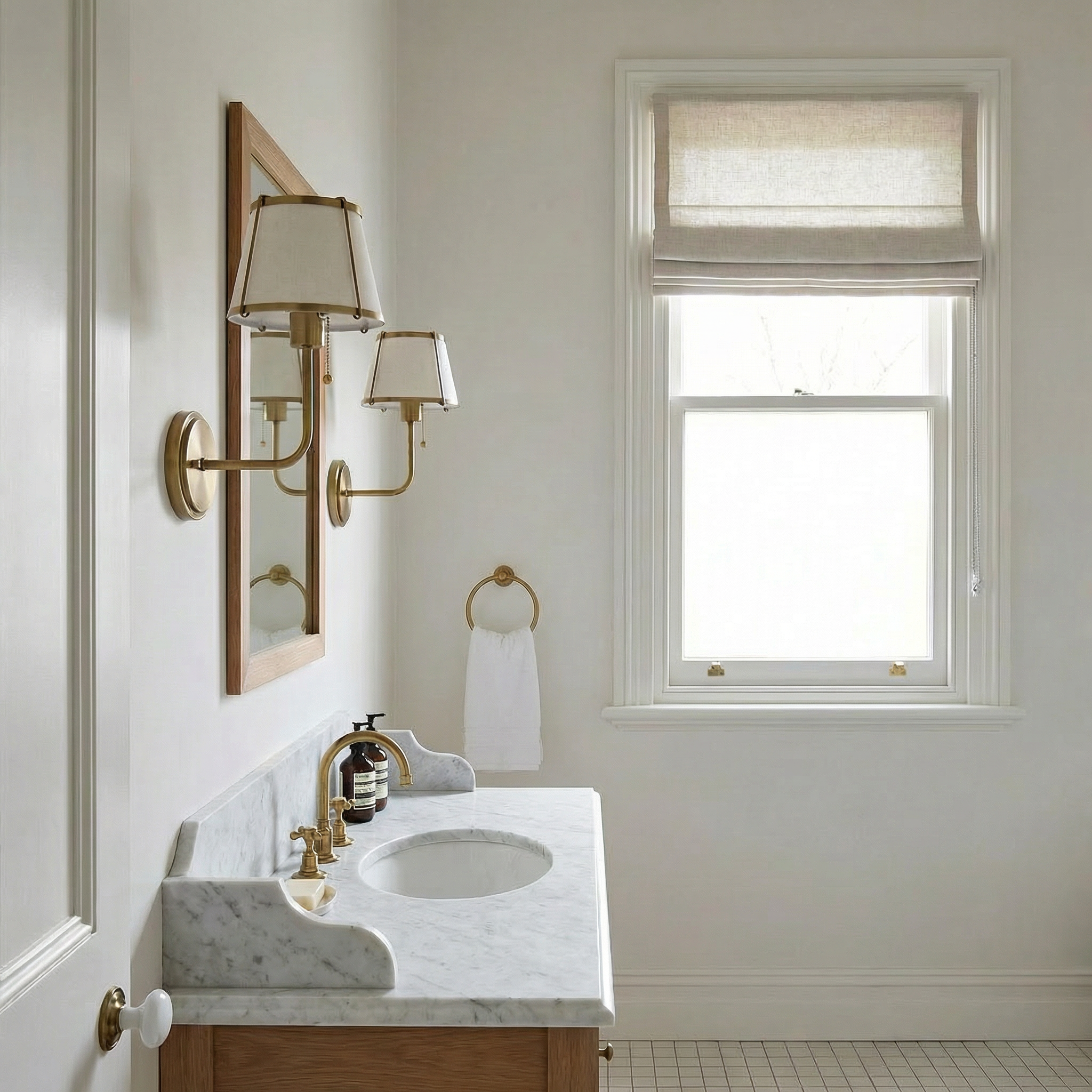 Traditional aged brass wall light with fabric shade mounted beside a timber-framed mirror above a marble vanity in a Tasmanian Federation-era bathroom with painted woodwork, Roman blind, and period brass fittings.